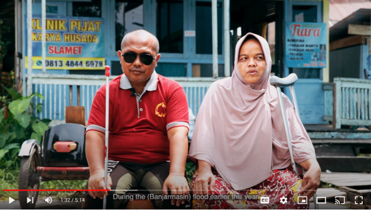 Photograph of two people from the video sat side-by-side. One is wearing dark glasses, the other is holding crutches Cover Image