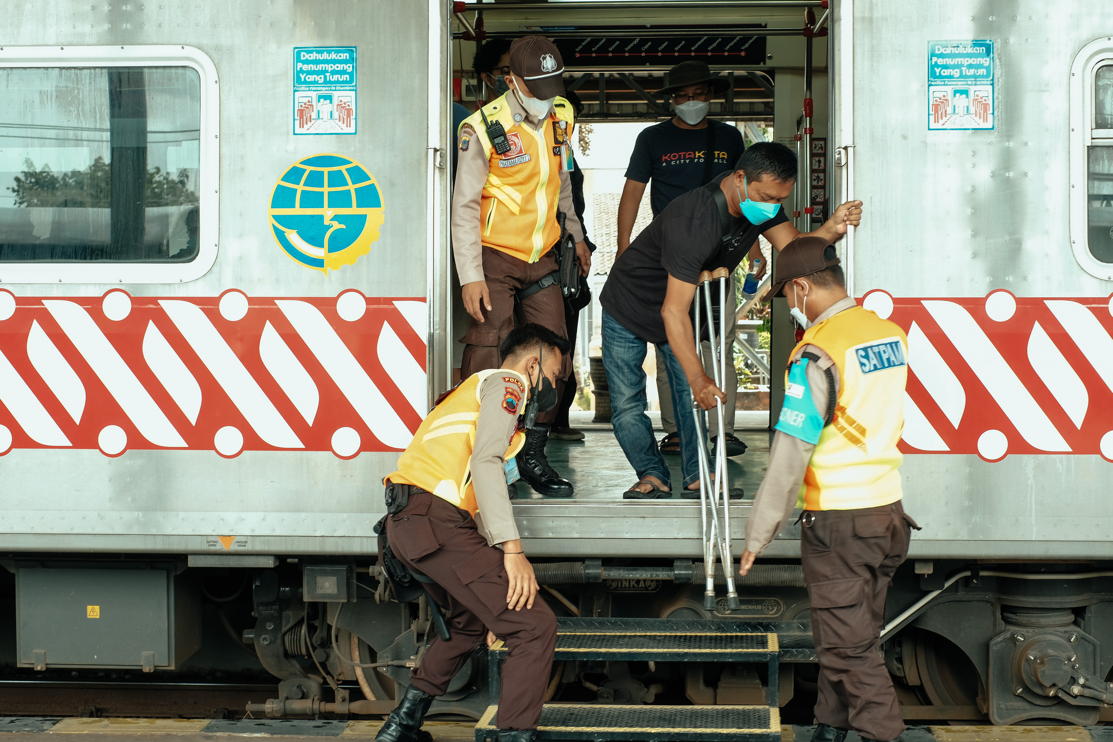 A man using crutches is stepping down from a high train with the help of 3 workers Cover Image