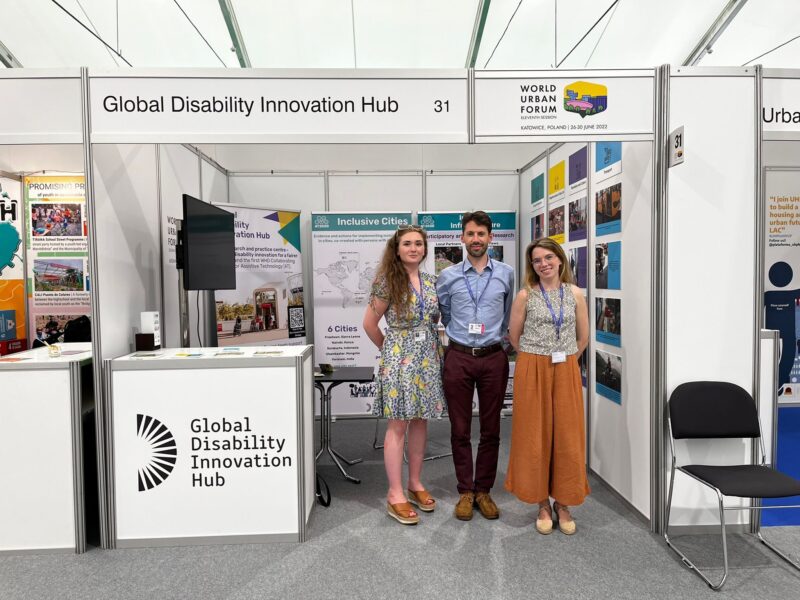 Photograph of the 3 inclusive design team members stood in front of the GDI Hub stand at the World Urban Forum conference Cover Image