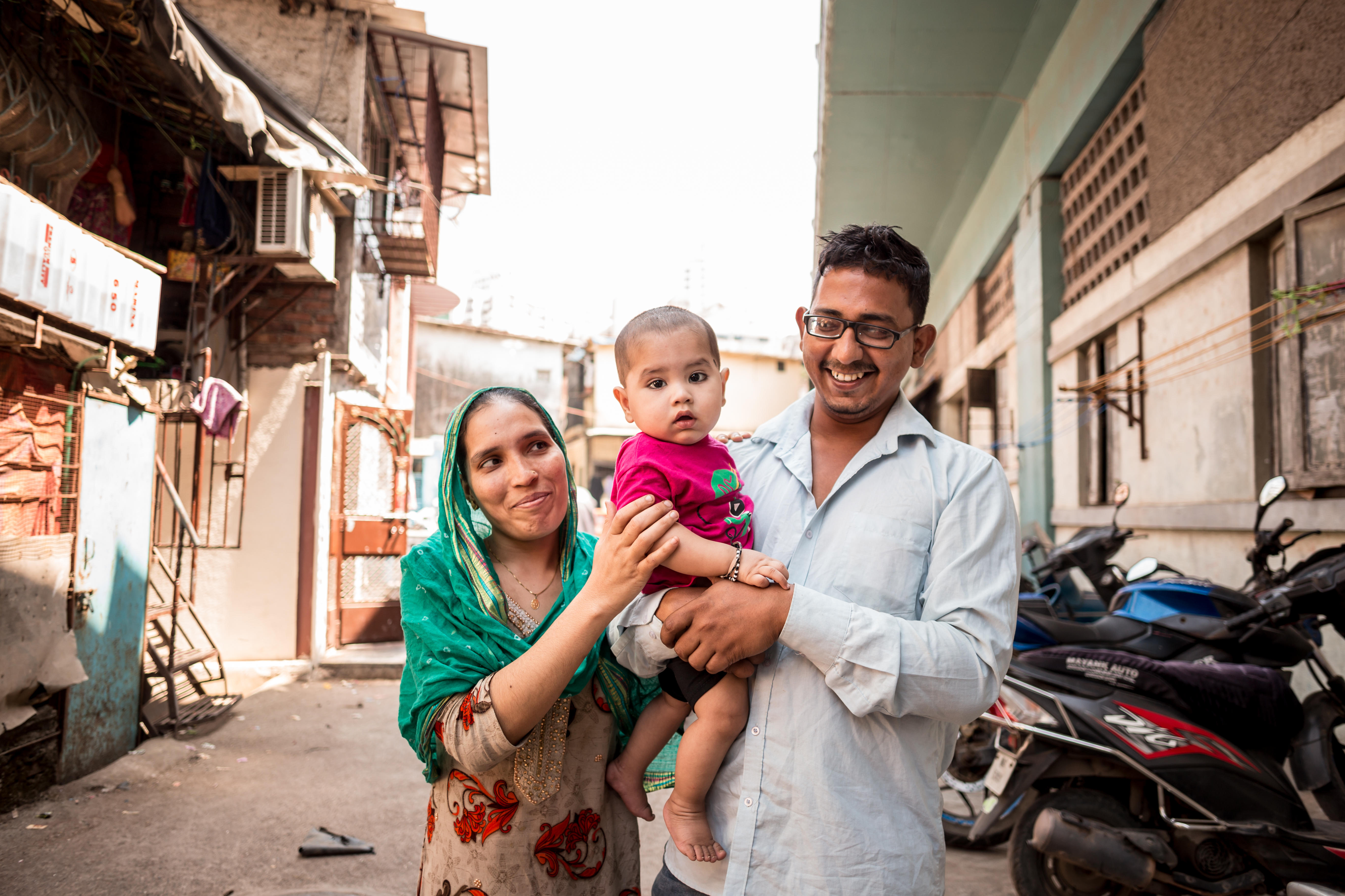 A mother and father holding a baby, smiling