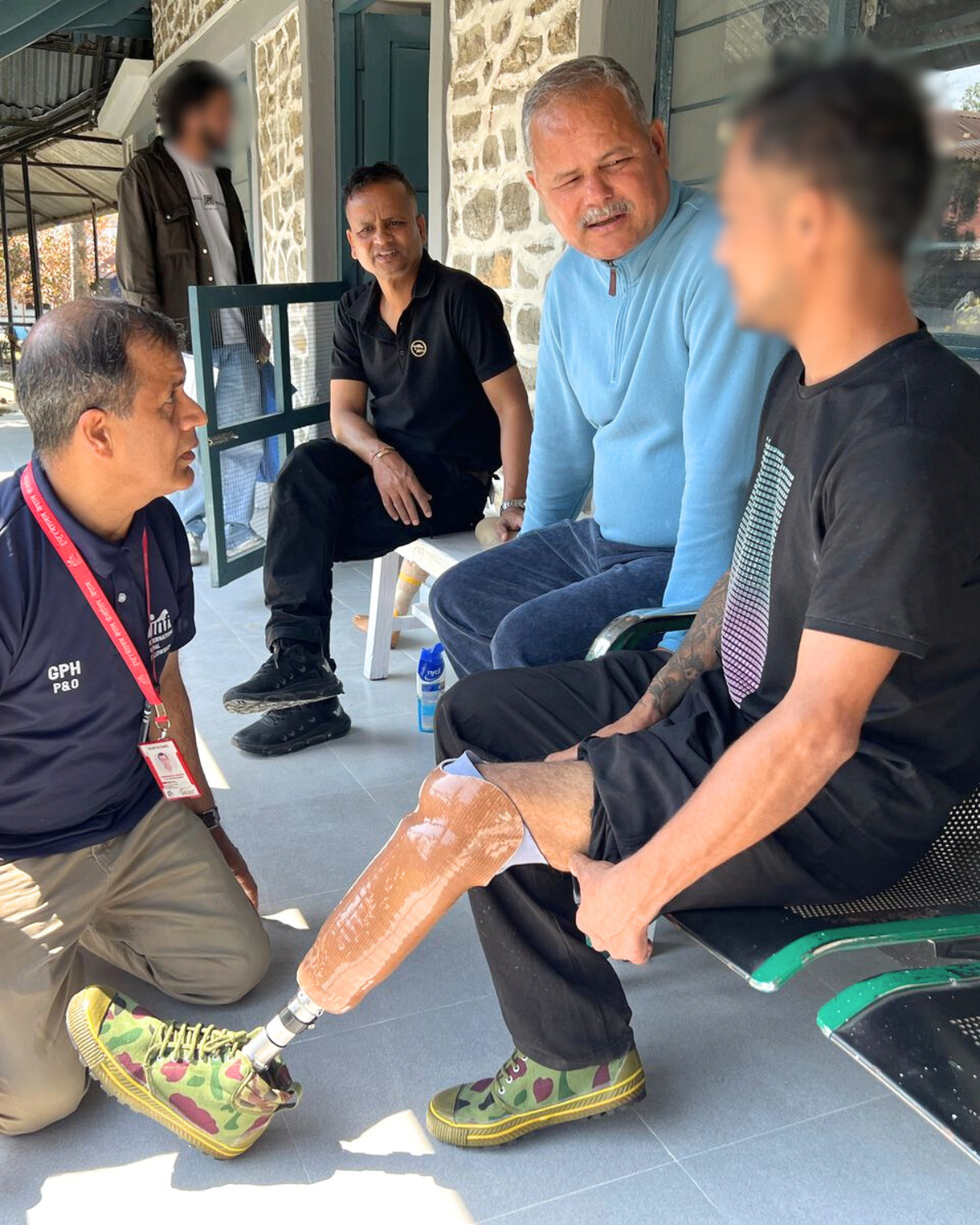 A person sitting on a bench being fitted with a liner and prosthetic leg. They are talking to a clinician and have other participants and clinicians nearby. Cover Image
