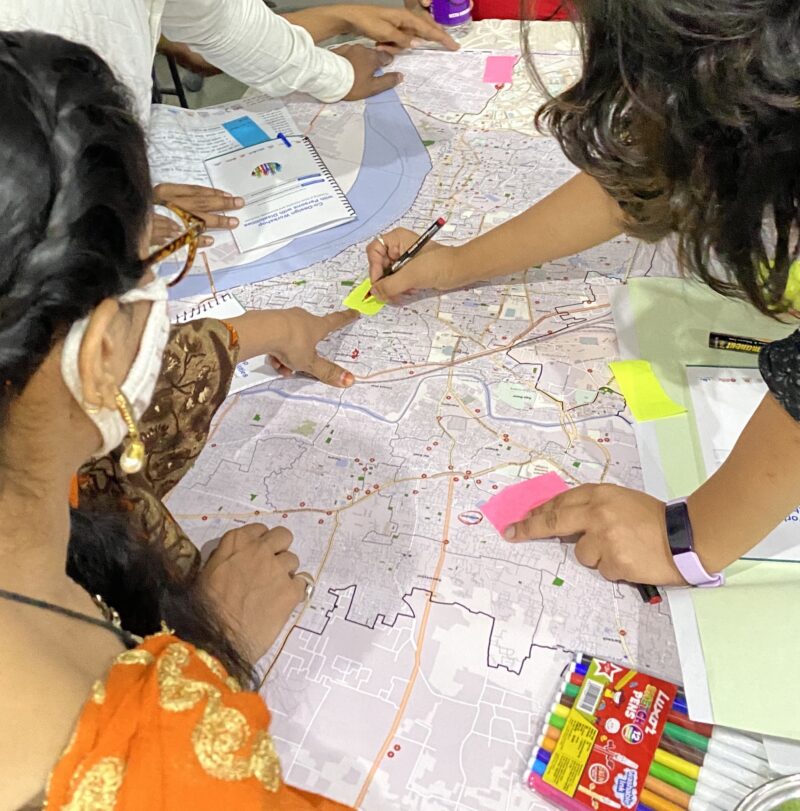 a group of people stand around a map, pointing and labelling certain areas Cover Image