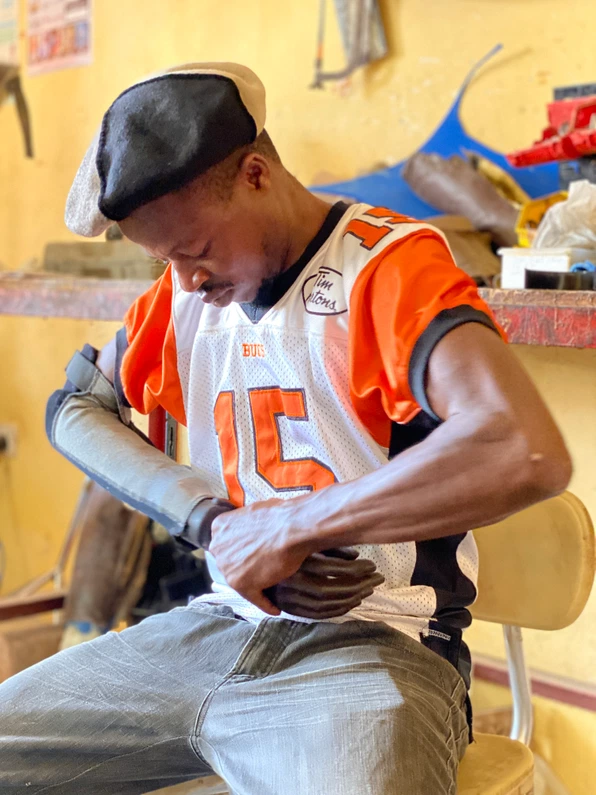 Young man sitting looking at new prosthetic arm - developed at low cost Cover Image